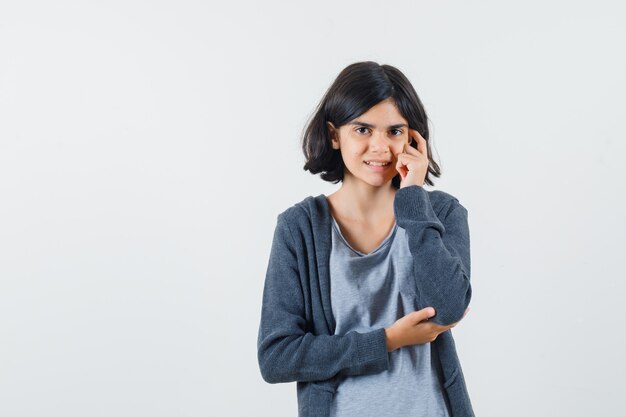 Niña de pie en pose de pensamiento en camiseta, chaqueta y aspecto sensible