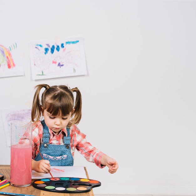 Niña pintando con acuarela en mesa de madera