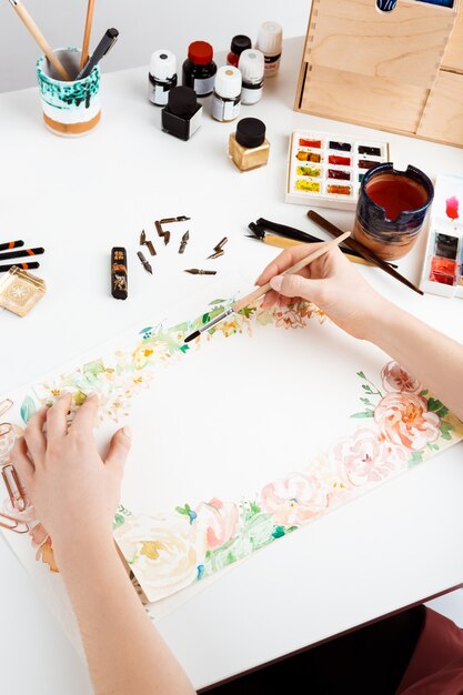 Niña pintando flores sobre papel con acuarela.