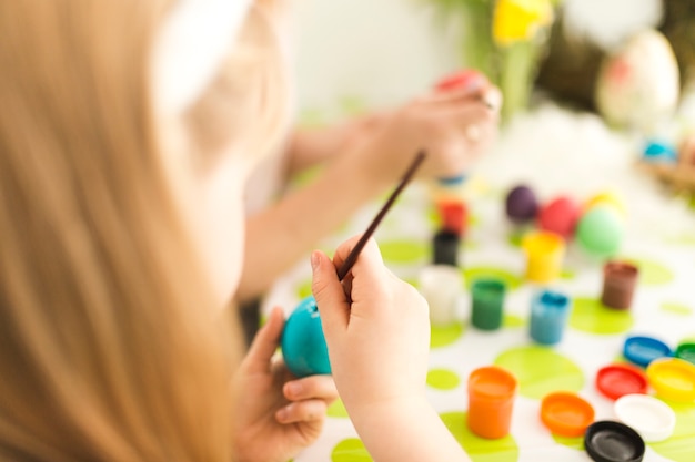 Niña pintando huevo con madre