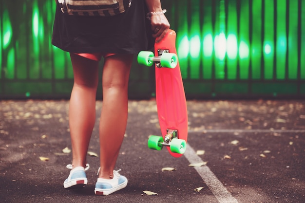 Niña con plástico naranja penny shortboard detrás de la pared verde en la tapa