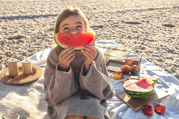 Foto gratuita una niña en una playa de arena come una sandía