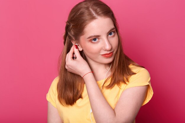 la niña se pone los auriculares, está lista para escuchar música, usa una camiseta amarilla brillante, tiene el cabello castaño y liso, pasa tiempo libre sola. Concepto de personas y entairtaiment.