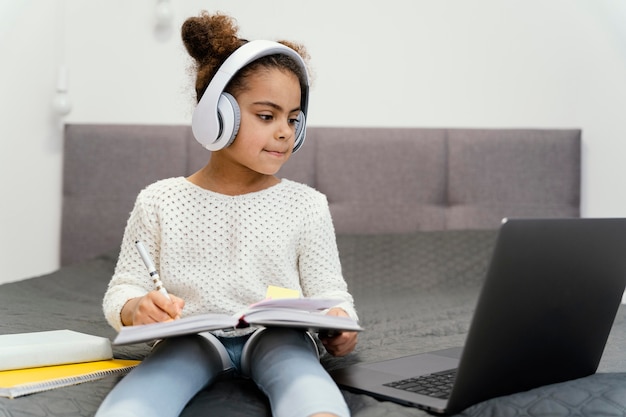 Niña con portátil y auriculares para la escuela en línea