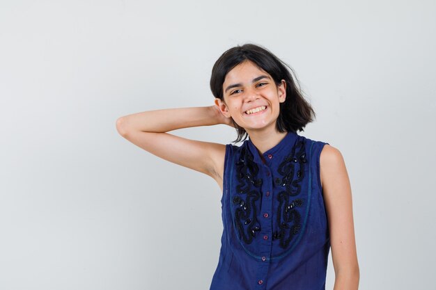 Niña posando con la mano en el pelo en blusa azul y mirando alegre.