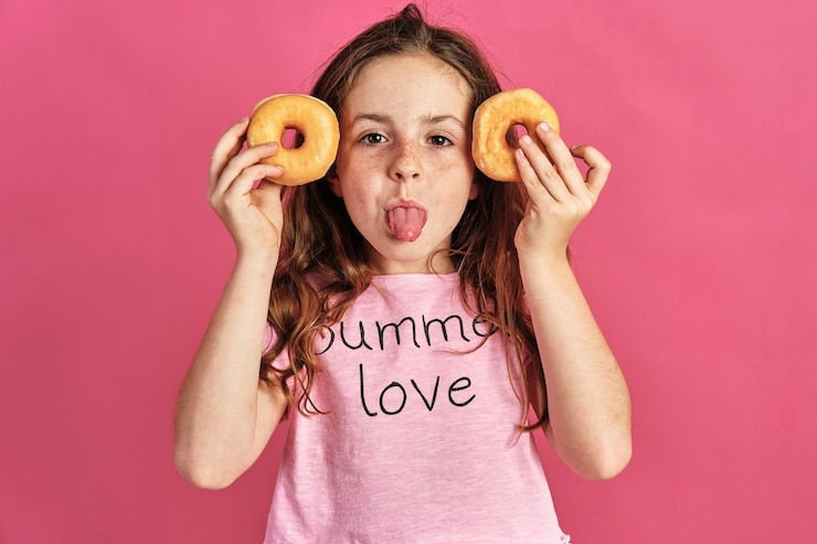 Foto gratuito niña posando con un par de rosquillas en una pared rosa