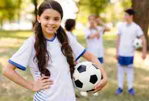 Foto gratuita niña posando con una pelota de fútbol fuera