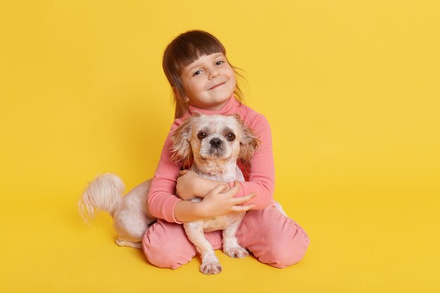 Niña posando con perro pequinés en amarillo