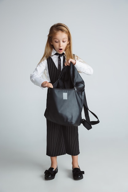 Niña posando en uniforme escolar con mochila en pared blanca