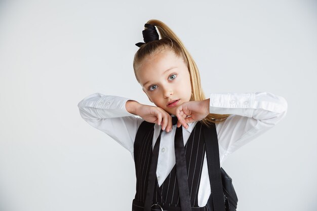 Niña posando en uniforme escolar con mochila en pared blanca