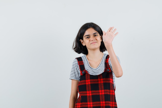 Niña preadolescente agitando la mano para saludar en camiseta, mono, vista frontal.