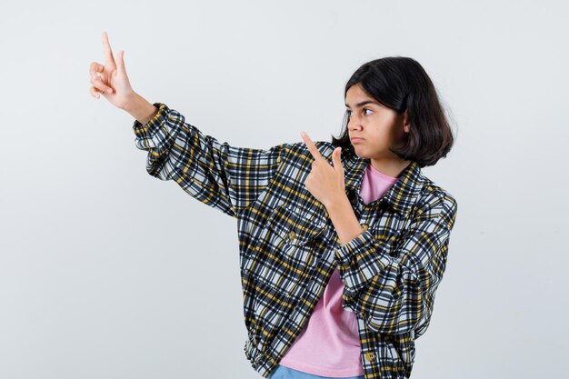 Niña preadolescente apuntando a un lado en camisa, vista frontal de la chaqueta.