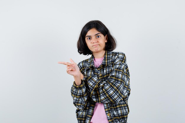 Niña preadolescente apuntando a un lado en camisa, vista frontal de la chaqueta.