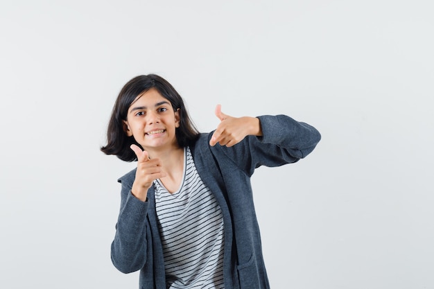 Niña preadolescente en camisa, chaqueta apuntando a la cámara y mirando optimista