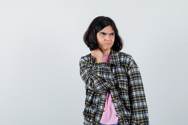 Foto gratuita niña preadolescente en camisa, chaqueta masajeando su cuello mientras mira a un lado y mira preocupada, vista frontal.