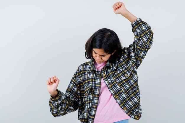 Niña preadolescente en camisa, chaqueta mostrando gesto de ganador con las manos arriba, vista frontal.