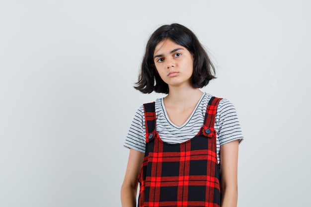 Foto gratuita niña preadolescente en camiseta, mono de pie delante de la cámara y mirando serio