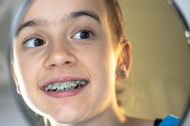 Niña preadolescente caucásica con aparatos dentales mirándose en el espejo