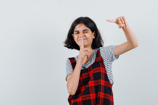 Niña preadolescente mostrando gesto silencioso mientras apunta a un lado en camiseta