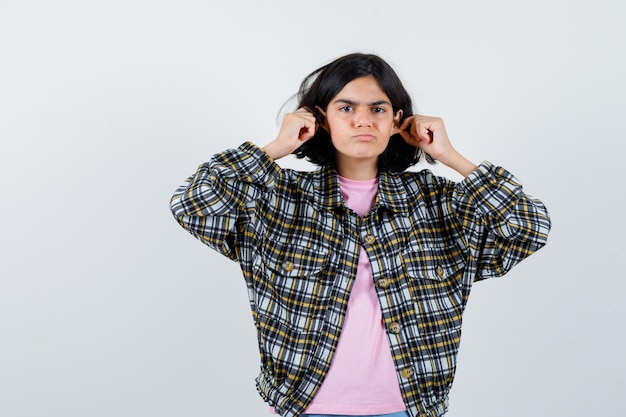 Niña preadolescente pellizcando sus orejas en camisa, vista frontal de la chaqueta.