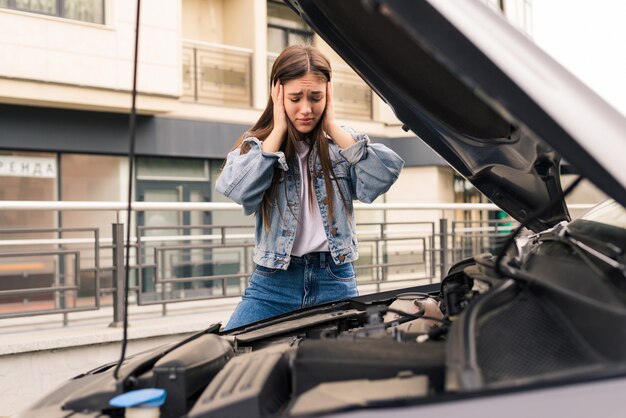 Niña preocupada está usando un teléfono para explicarle al mecánico el problema con un automóvil que tiene.