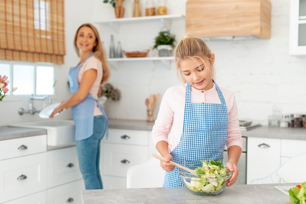 Niña preparando ensalada supervisada por su madre
