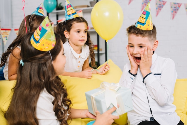 Niña que da una caja de regalo envuelta al chico de cumpleaños sorprendido en la fiesta