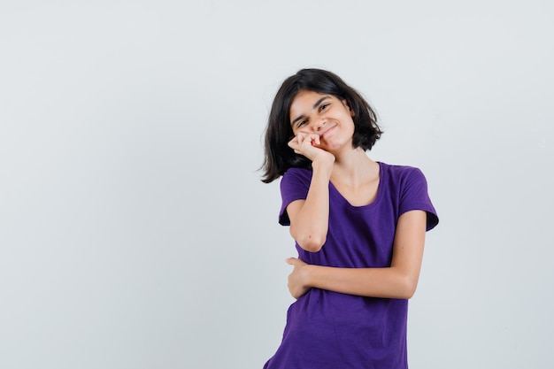 Niña que se inclina la mejilla en la palma en camiseta y se ve bonita.