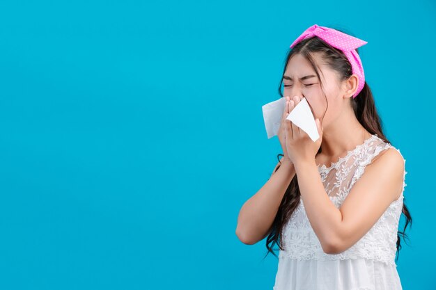 La niña que lleva un pijama blanco no se siente cómoda. Usando pañuelos para limpiarse la nariz con un azul.