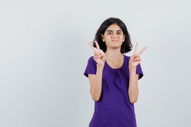 Niña que muestra el signo de la victoria en camiseta y parece confiada.