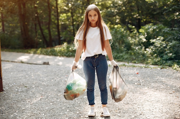 Foto gratuita niña recoge basura en bolsas de basura en el parque