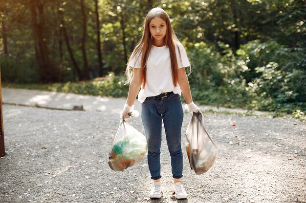 Niña recoge basura en bolsas de basura en el parque