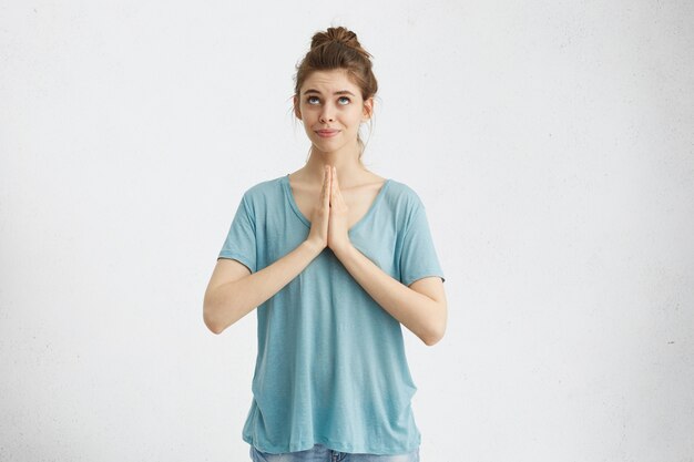 Niña religiosa con el pelo recogido en nudos, juntando las palmas de las manos y mirando hacia arriba, rezando a Dios, pidiendo perdón o pidiendo que su sueño se haga realidad. Emociones y sentimientos humanos