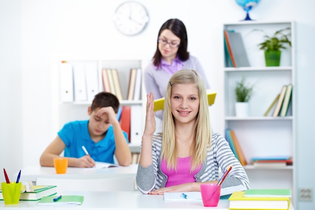 Niña rubia con el brazo levantado en clase