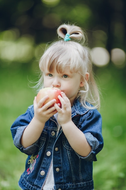 Niña rubia pequeña mordiendo una manzana