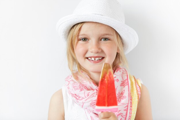 Niña rubia con sombrero blanco y comiendo helado