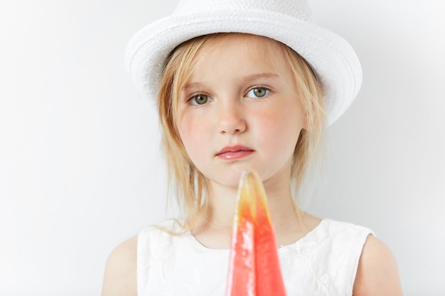 Niña rubia con sombrero blanco y sosteniendo paleta