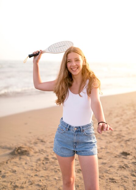 Niña rubia sonriente jugando al tenis en la playa