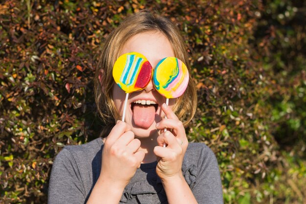 Niña sacando la lengua con piruletas frente a los ojos