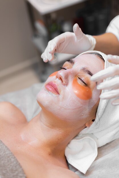 Una niña en un salón de belleza en una sala de cosmetología yace en una cama se relaja con una máscara en la cara y parches debajo de los ojos