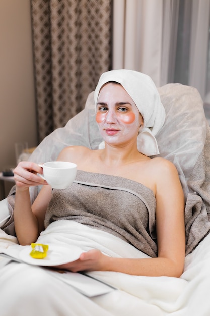 Una niña en un salón de belleza en una sala de cosmetología yace en una cama se relaja con una máscara en la cara y parches debajo de los ojos