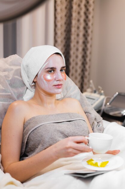 Una niña en un salón de belleza en una sala de cosmetología yace en una cama se relaja con una máscara en la cara y parches debajo de los ojos