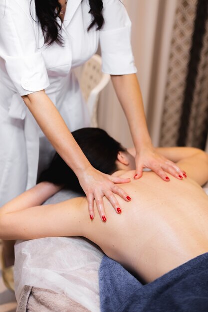 La niña en el salón de spa recibe un masaje de espalda y cuello, se acuesta en la mesa de cosmetología, se relaja y disfruta del proceso.