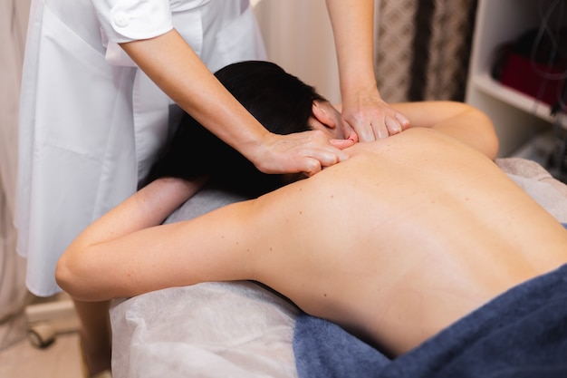 La niña en el salón de spa recibe un masaje de espalda y cuello, se acuesta en la mesa de cosmetología, se relaja y disfruta del proceso.