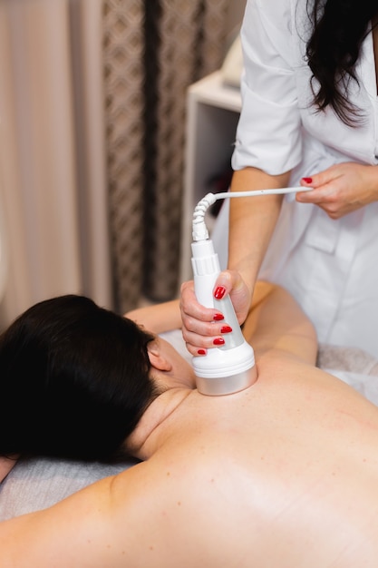 La niña en el salón de spa recibe un masaje de espalda y cuello, se acuesta en la mesa de cosmetología, se relaja y disfruta del proceso.