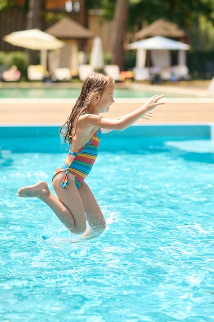 Una niña saltando al agua en la piscina.