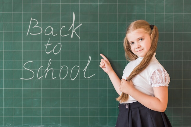 Foto gratuita niña señalando a la escuela con letras en el tablero trasero