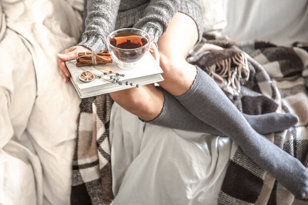 niña sentada en una acogedora cama caliente con té y un libro, el concepto de comodidad y hipster