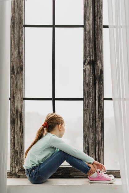 Niña sentada en el alféizar de una ventana