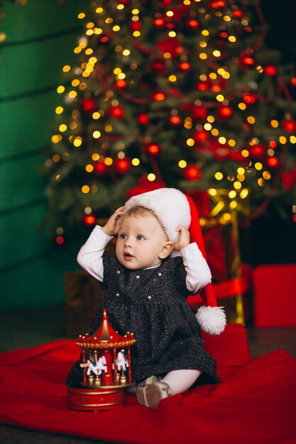 Niña sentada por el árbol de navidad con el juguete